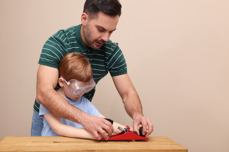Father teaching son how to work with plane near beige wallの写真素材
