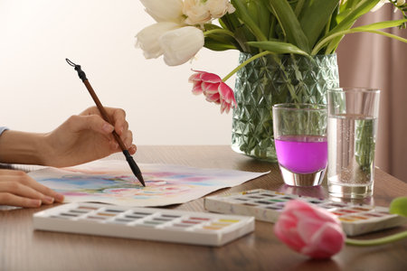 Woman painting flowers with watercolor at wooden table indoors, closeup. Creative artworkの写真素材