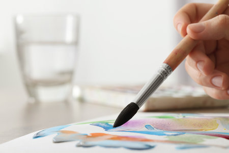 Woman painting with watercolor at wooden table indoors, closeup. Space for textの写真素材