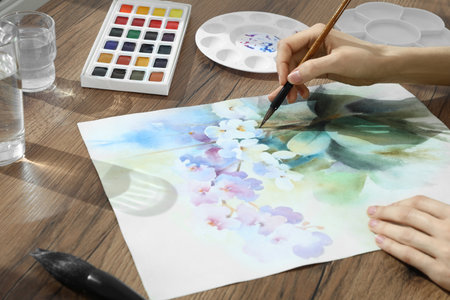 Woman painting flowers with watercolor at wooden table, closeup. Creative artworkの写真素材
