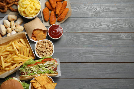 French fries, onion rings and other fast food on gray wooden table, flat lay with space for text
