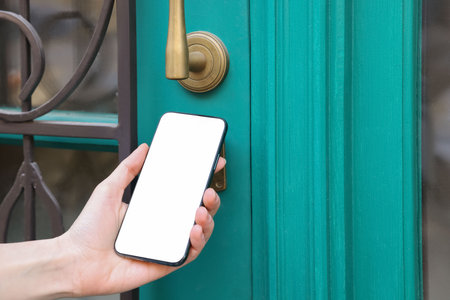 Woman opening door with smartphone outdoors, closeupの写真素材