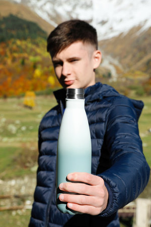 Boy holding thermo bottle with drink in mountains, focus on handの写真素材