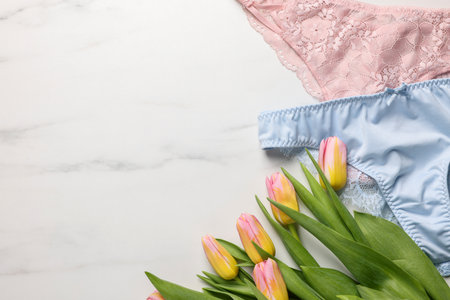 Elegant women's underwear and beautiful tulips on white marble background, flat lay. Space for textの写真素材