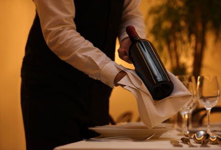 Butler holding bottle of wine near table in restaurant, closeupの写真素材