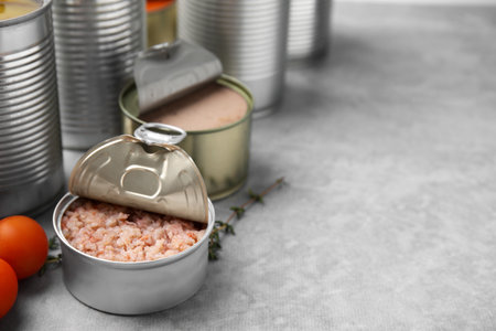 Open tin cans with different preserved products on gray table, closeup. Space for textの写真素材