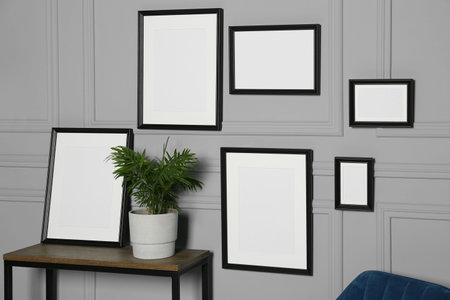 Empty frames hanging on gray wall near wooden table indoors