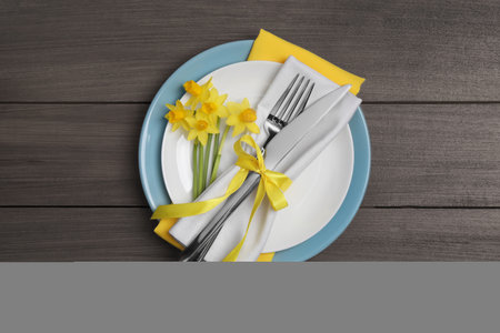 Festive table setting with narcissuses and cutlery on wooden background, top view. Easter celebrationの写真素材