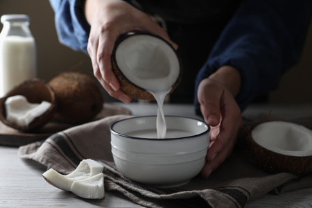 Woman pouring coconut milk into bowl at white wooden table, closeupの写真素材