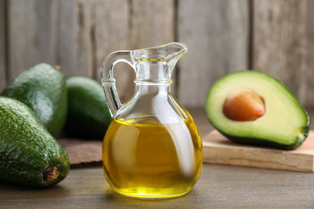 Jug with oil and ripe fresh avocados on wooden table, closeupの写真素材