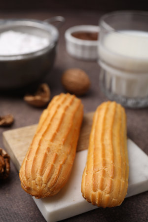 Delicious eclairs, walnuts and milk on gray table, closeup