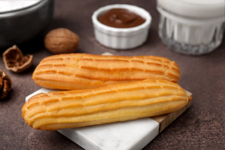 Delicious eclairs, walnuts and chocolate paste on gray table, closeup
