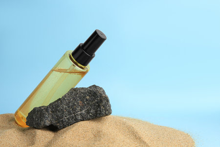 Bottle with serum and stone on sand against light blue background, space for text. Cosmetic productの写真素材