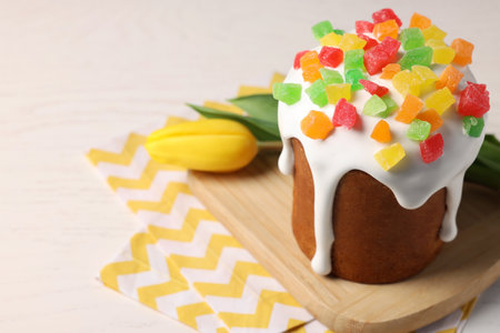 Delicious Easter cake with pieces of candied fruits and tulip on white table, closeup. Space for...