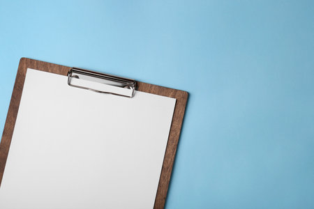 New wooden clipboard with sheet of blank paper on light blue background, top view. Space for textの写真素材