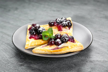 Fresh tasty puff pastry with sugar powder, jam, sweet berries and mint on gray table