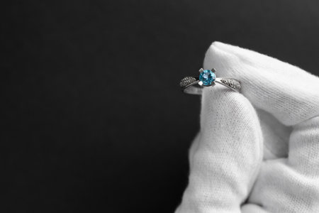 Jeweler holding topaz ring on dark gray background, closeup. Space for textの写真素材