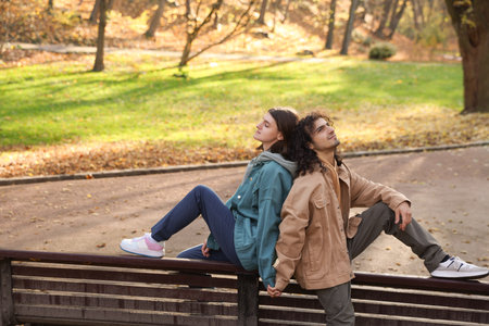 Young couple sitting on wooden bench in autumn park. Dating agencyの写真素材