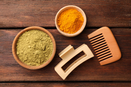 Hair care products. Comb, hair clip, henna and turmeric powder on wooden table, flat layの写真素材