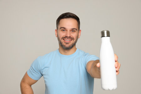 Happy man showing thermo bottle on light gray backgroundの写真素材