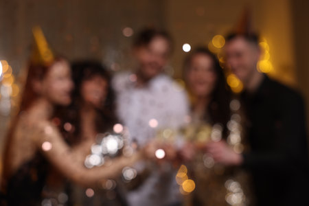 Blurred view of happy friends clinking glasses of sparkling wine at birthday party indoorsの写真素材