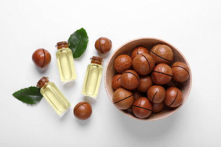 Delicious organic Macadamia nuts, green leaves and natural oil on white background, flat layの写真素材
