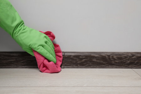 Woman in gloves cleaning plinth with cloth indoors, closeup. Space for textの写真素材