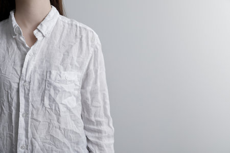 Woman wearing wrinkled white blouse on light gray background, closeup. Space for text