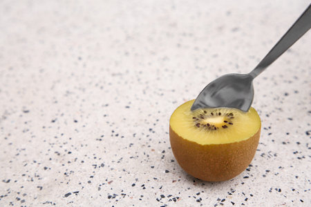 Spoon in fresh ripe yellow kiwi on white table with pattern. Space for textの写真素材