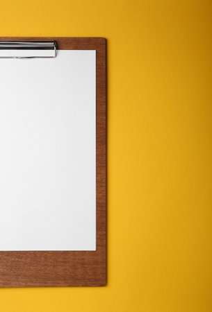 Wooden clipboard with sheet of blank paper on yellow background, top view. Space for text