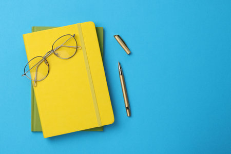 Ballpoint pen, notebooks and glasses on light blue background, flat lay. Space for textの写真素材