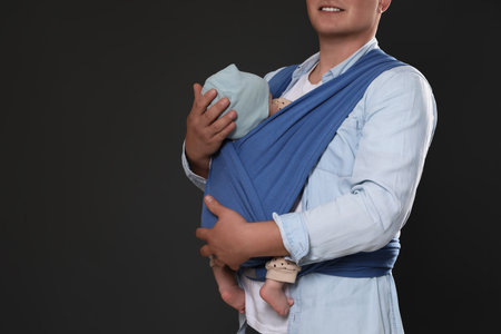 Father holding his child in sling (baby carrier) on black background, closeup. Space for textの写真素材