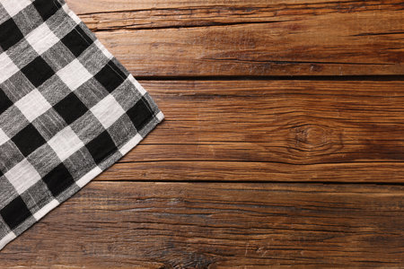 Black checkered tablecloth on wooden table, top view. Space for text