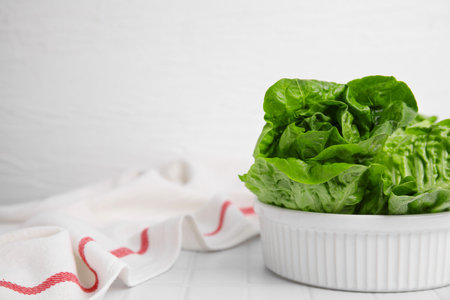 Bowl with fresh green romaine lettuces on white tiled table, space for textの写真素材