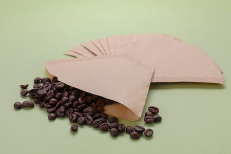 Paper coffee filters and scattered beans on pale olive backgroundの写真素材