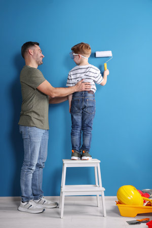 Father and son painting wall with roller indoors, back view. Repair workの写真素材