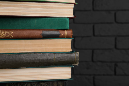 Many old hardcover books near black brick wall, closeup. Space for textの写真素材