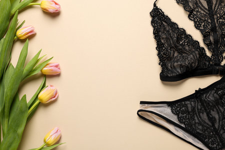 Elegant black women's underwear and beautiful tulips on beige background, flat lay. Space for textの写真素材