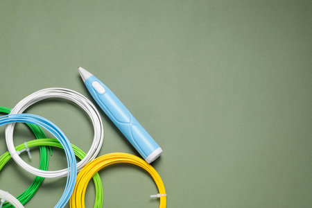 Stylish 3D pen and colorful plastic filaments on khaki background, flat lay. Space for text