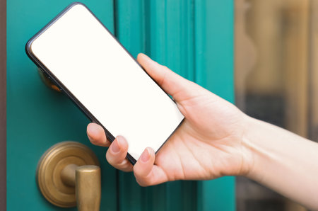 Woman opening door with smartphone outdoors, closeupの写真素材