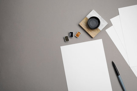 Blank sheets of paper, watercolor paints and brush on gray table, flat lay. Space for textの写真素材