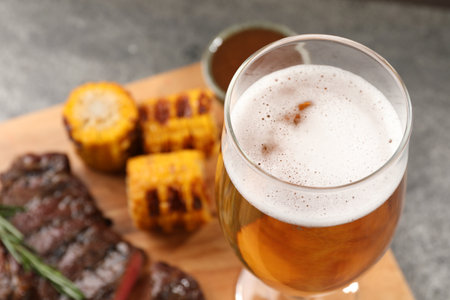 Glass of beer, delicious fried steak and corn on gray table, closeup. Space for textの写真素材