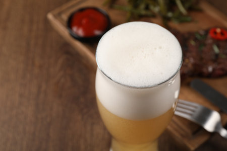 Glass of beer, delicious fried steak and sauce on wooden table, closeup. Space for textの写真素材