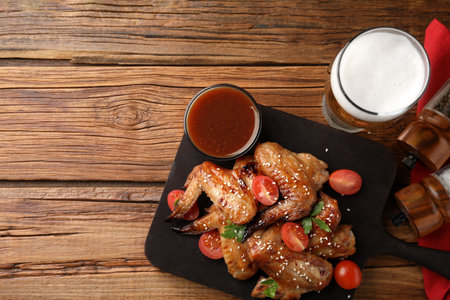 Glass of beer, delicious baked chicken wings and sauce on wooden table, flat lay. Space for textの写真素材