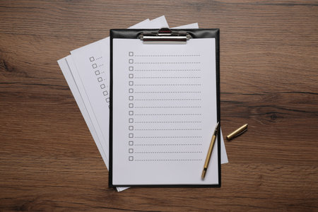 Clipboard with checkboxes and pen on wooden table, flat lay