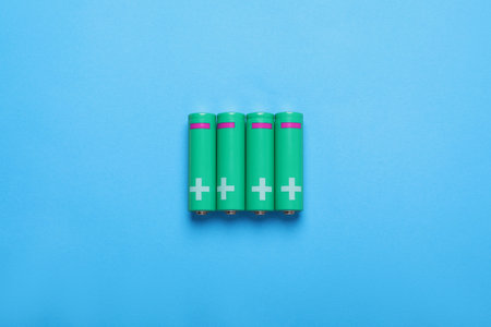 New AA size batteries on light blue background, flat lay