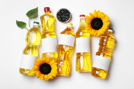 Bottles of sunflower cooking oil, seeds and beautiful flowers on white background, flat layの写真素材