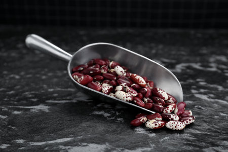Metal scoop with dry kidney beans on black textured table