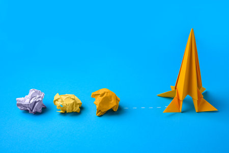 Handmade orange rocket and crumpled pieces of paper on light blue background