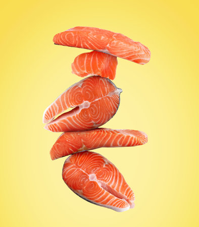 Cut fresh salmon falling on yellow backgroundの写真素材